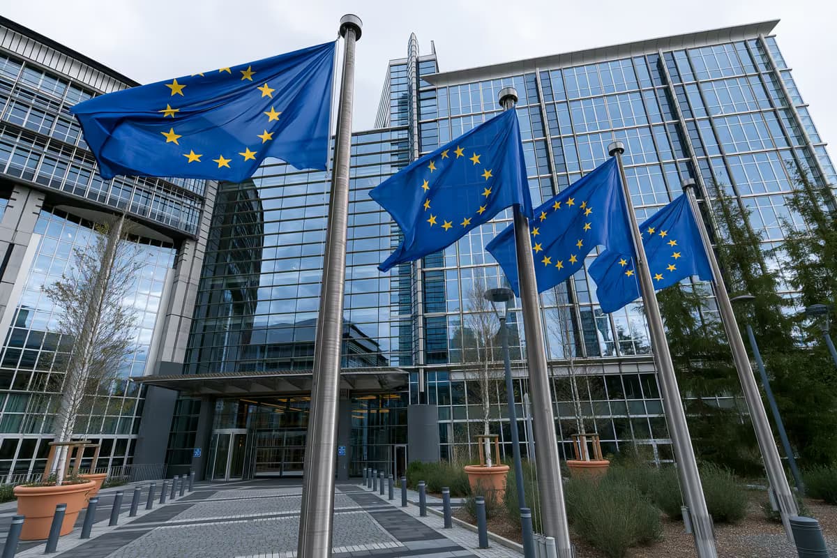 Σημαίες της Ευρωπαϊκής Ένωσης σε κοντάρια μπροστά από ένα σύγχρονο γυάλινο κτίριο.
